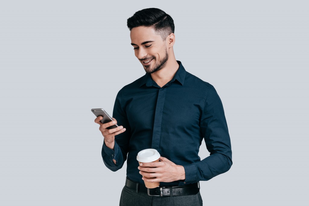 man with coffee looking through his phone